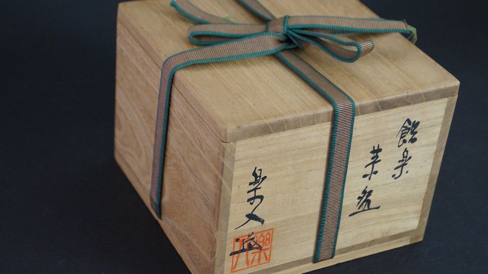 Geschlossene, mit gruen-braunem Band verschnuerte Aufbewahrungsbox der Chawan aus Raku-Keramik