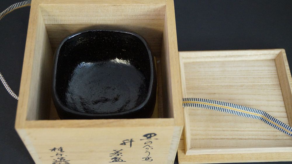 Chawan aus Raku-Keramik in der geoeffneten Aufbewahrungsbox neben dem beschrifteten Kastendeckel