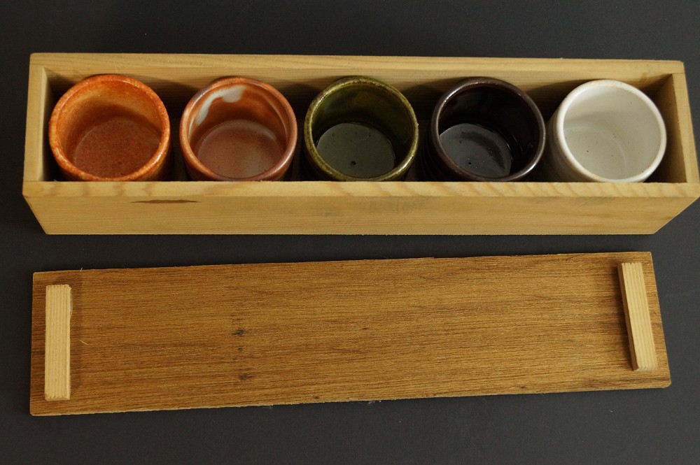 Fuenf Sakeschalen nebeneinander in der laenglichen Holzbox neben dem Deckel Set in Aufbewahrungsbox