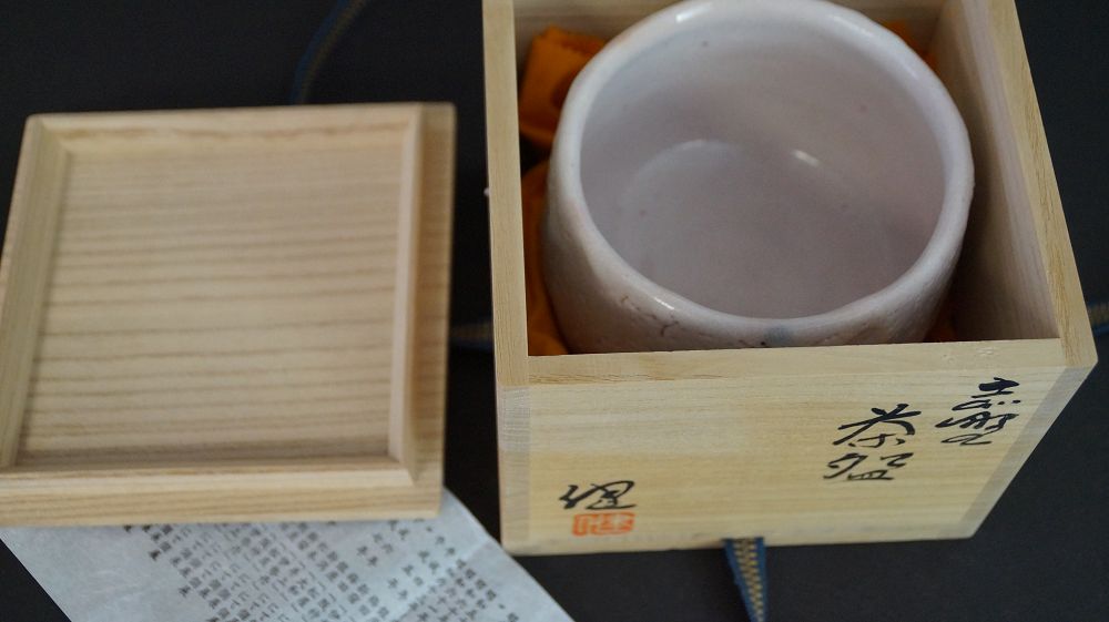 Chawan aus Shino-Keramik in der geoeffneten Aufbewahrungsbox neben dem Kastendeckel mit Kuenstlersignatur