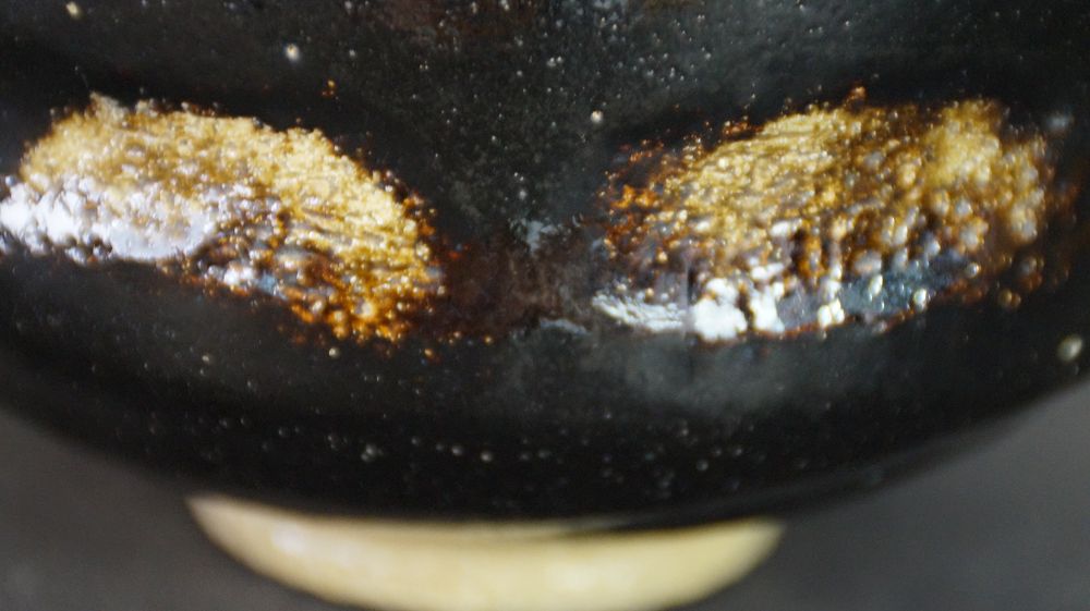 Gros plan extrême sur les deux taches de glaçure dorée sur la glaçure noire du chawan en céramique Raku