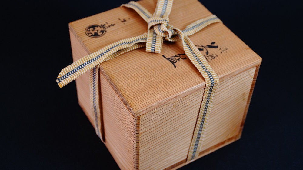 Geschlossene Aufbewahrungsbox der Chawan aus Raku-Keramik von Waraku Kawasaki mit Tuschebeschriftung und rundem Kuenstlersiegel, verschnuert mit gewebtem Band