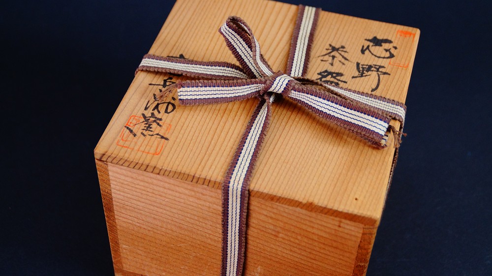 Geschlossene Aufbewahrungsbox der Chawan aus Shino-Keramik von Jyuzo Sato mit Tuschebeschriftung Shino Chawan und rotem Kuenstlersiegel, verschnuert mit gestreiftem Band