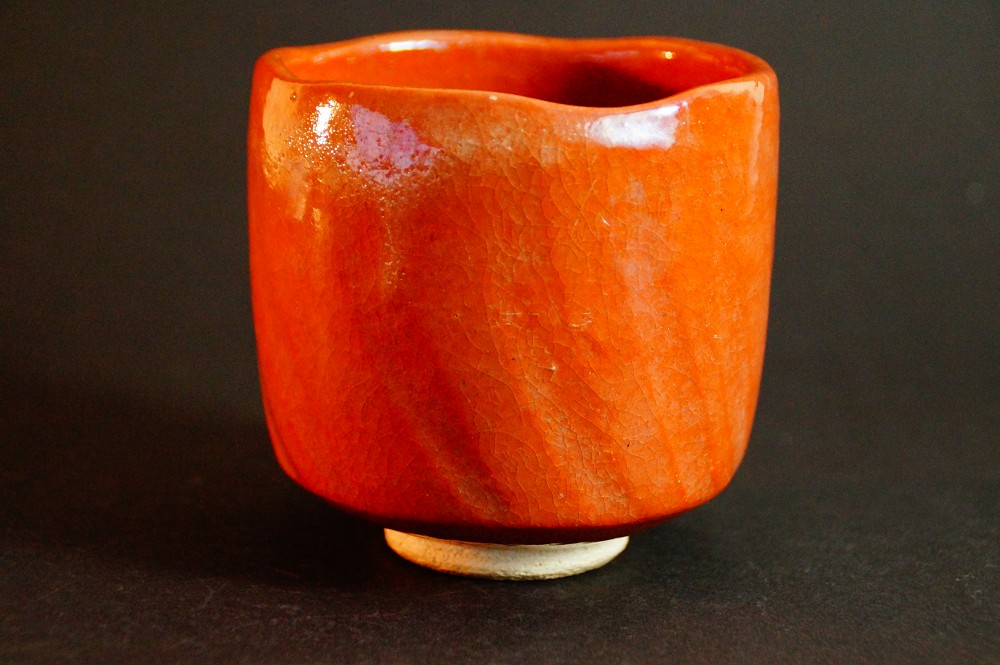 Seitenansicht des Chawan mit unregelmaessig geformtem Rand und roter Raku-Glasur von Seiraku