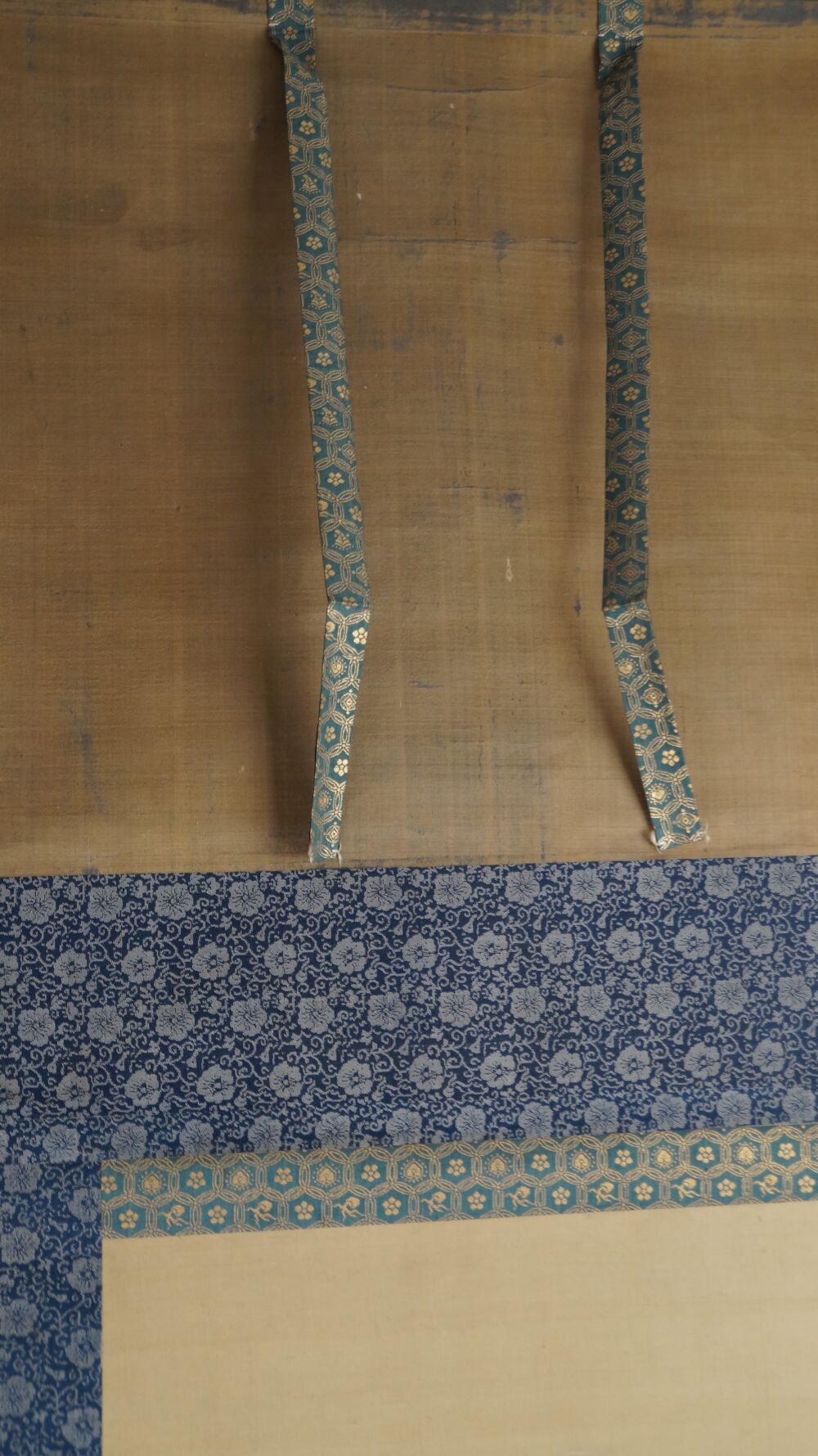 Detailansicht der Seidenmontierung mit Aufhaengebaendern und blauem Bluetenbrokat des Kakemono Bodhidharma auf dem Weg