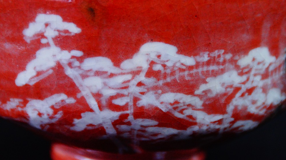 Nahaufnahme des weiss gemalten Kiefern- und Landschaftsmotivs auf der roten Glasur der Chawan aus Raku-Keramik von Waraku Kawasaki