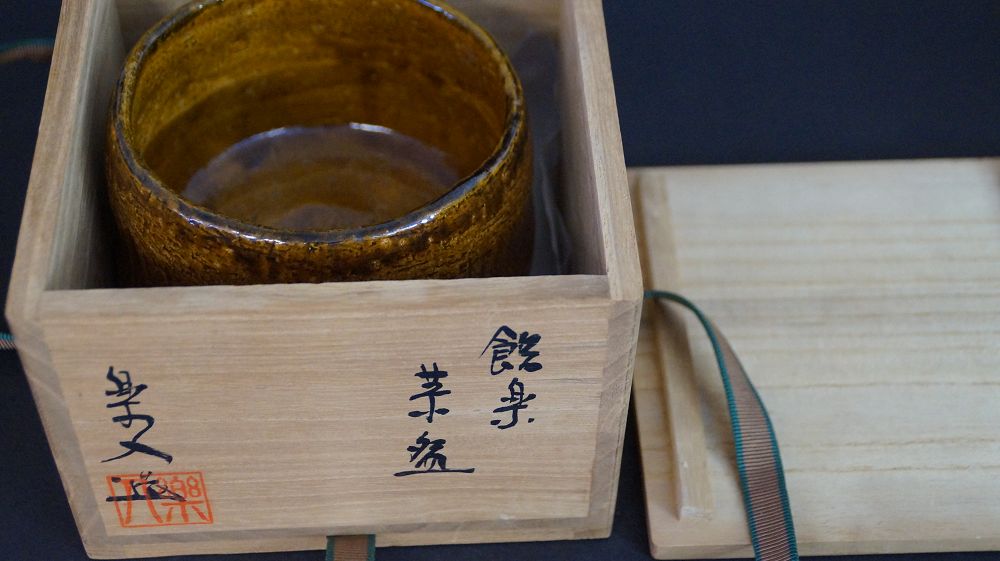 Chawan aus Raku-Keramik in der geoeffneten Aufbewahrungsbox neben dem beschrifteten Kastendeckel