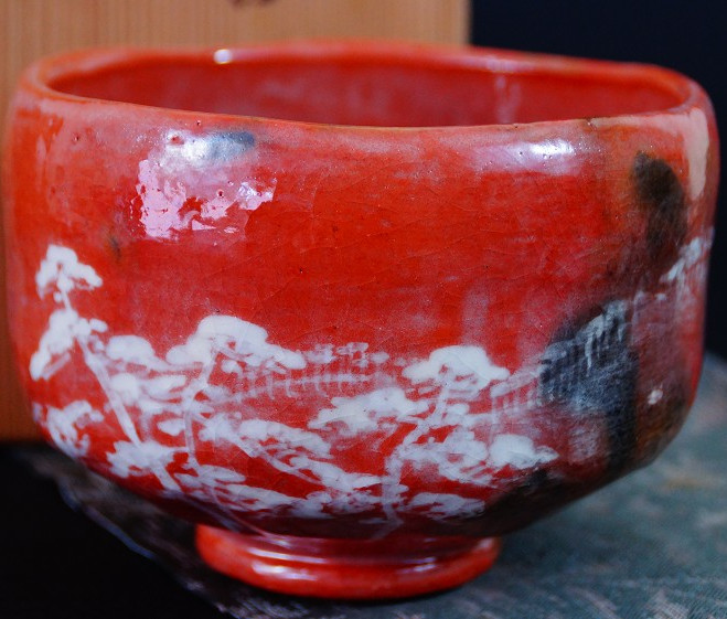 Chawan aus Raku-Keramik von Waraku Kawasaki mit leuchtend roter Glasur und weiss gemaltem Kiefernmotiv vor der Aufbewahrungsbox
