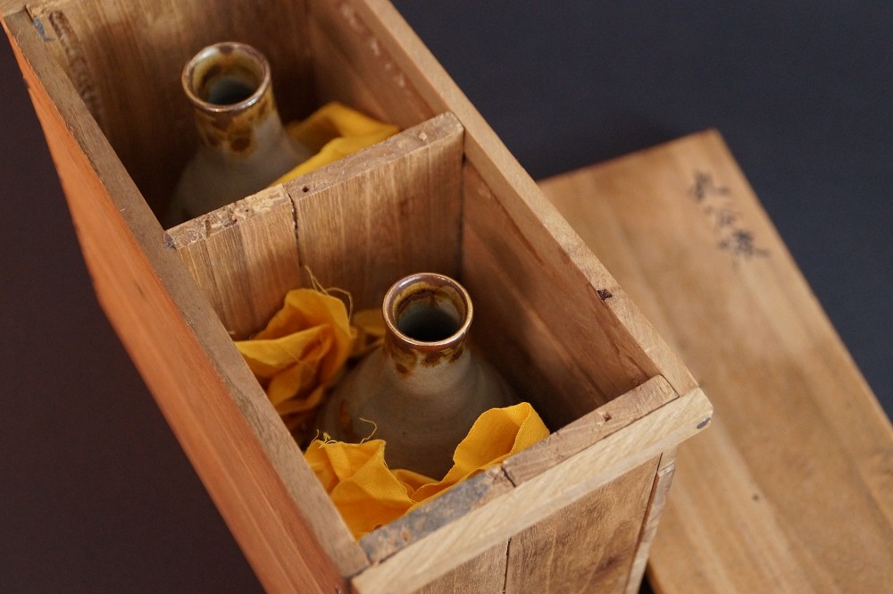 The two sake bottles nestled in orange cloth in the divided compartments of the storage box