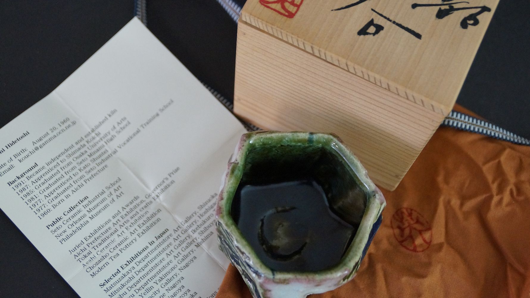 Guinomi Sake-Schale neben Aufbewahrungsbox und der Kuenstlerbiografie von Kawachi Hidetoshi