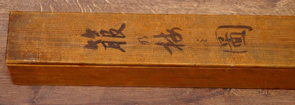 Primer plano de la inscripción a tinta y el sello rojo en la tapa de la caja de conservación