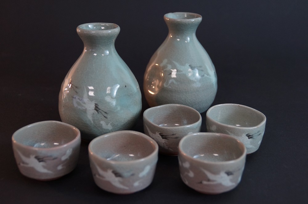 Frontalansicht des vollstaendigen Sets aus zwei Sake Flaschen und fuenf Sake Schalen mit Kranichmotiv