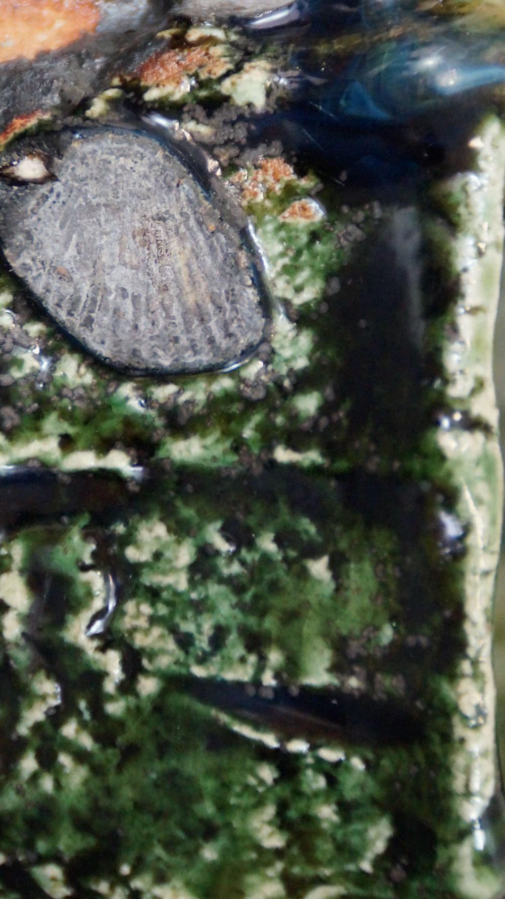Extreme Nahaufnahme der steinartigen Glasureinschluesse der Yunomi Tee-Schale aus Oribe-Keramik