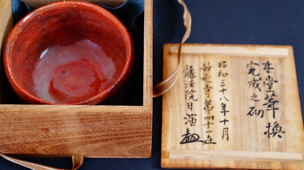 Cuenco de té de cerámica Raku de Sairi Hotoku junto a la tapa abierta de la caja de conservación con detallada inscripción a tinta