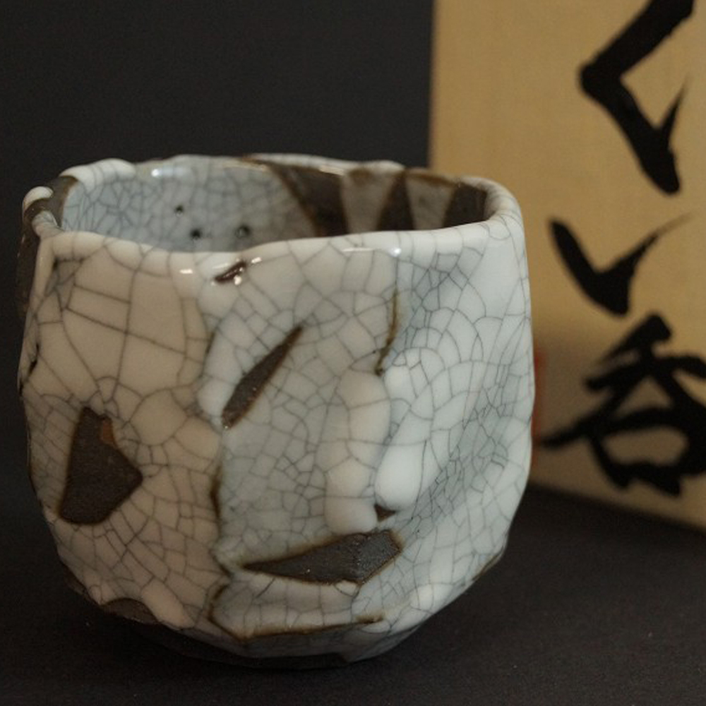 Coppa da sake Shino con smalto craquelé accanto alla scatola di conservazione con iscrizione anteprima primo piano del motivo