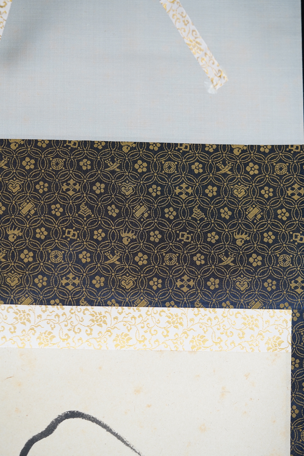 Detailansicht der dunkelblauen Seidenmontierung mit Goldmuster des Kakemono Daruma in Tusche