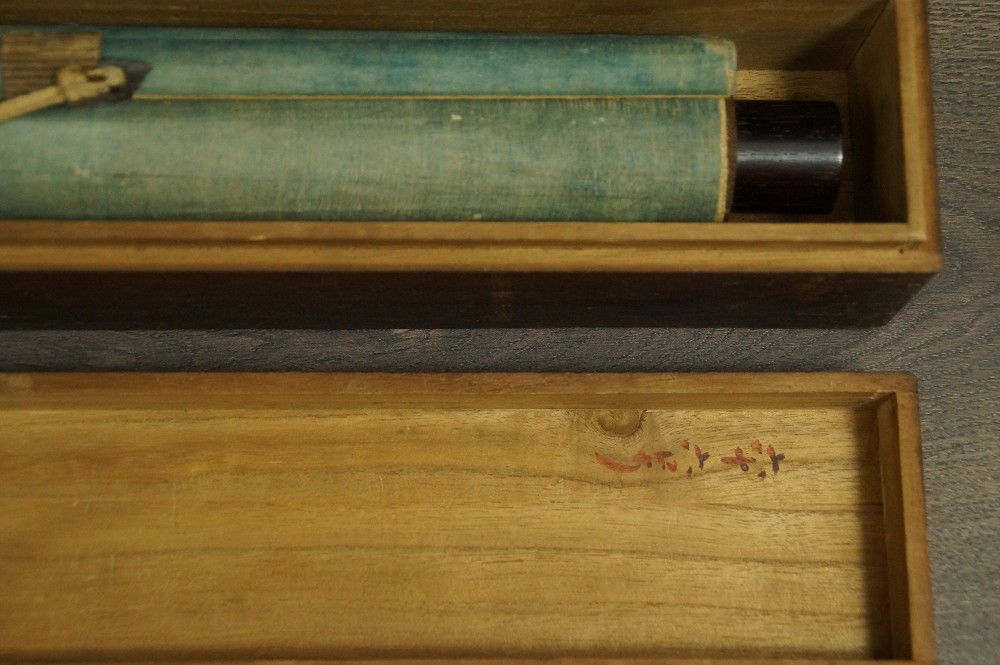 The rolled up hanging scroll with turquoise front fabric lying in the opened storage box